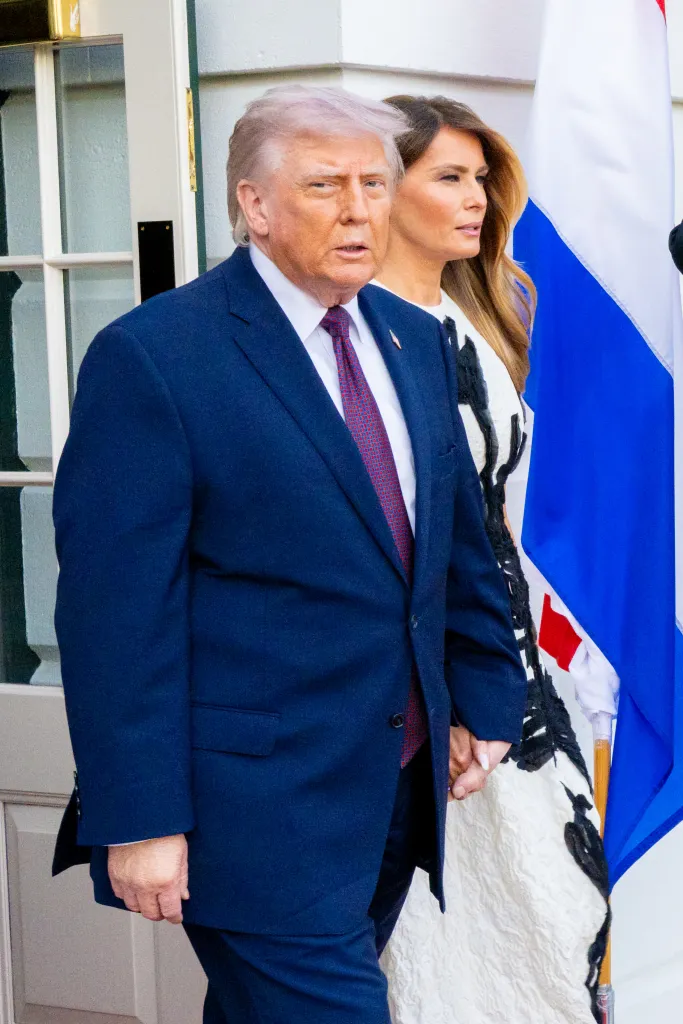 Donald and Melania Trump walk together outside the White House, with a Dutch flag visible in the background.