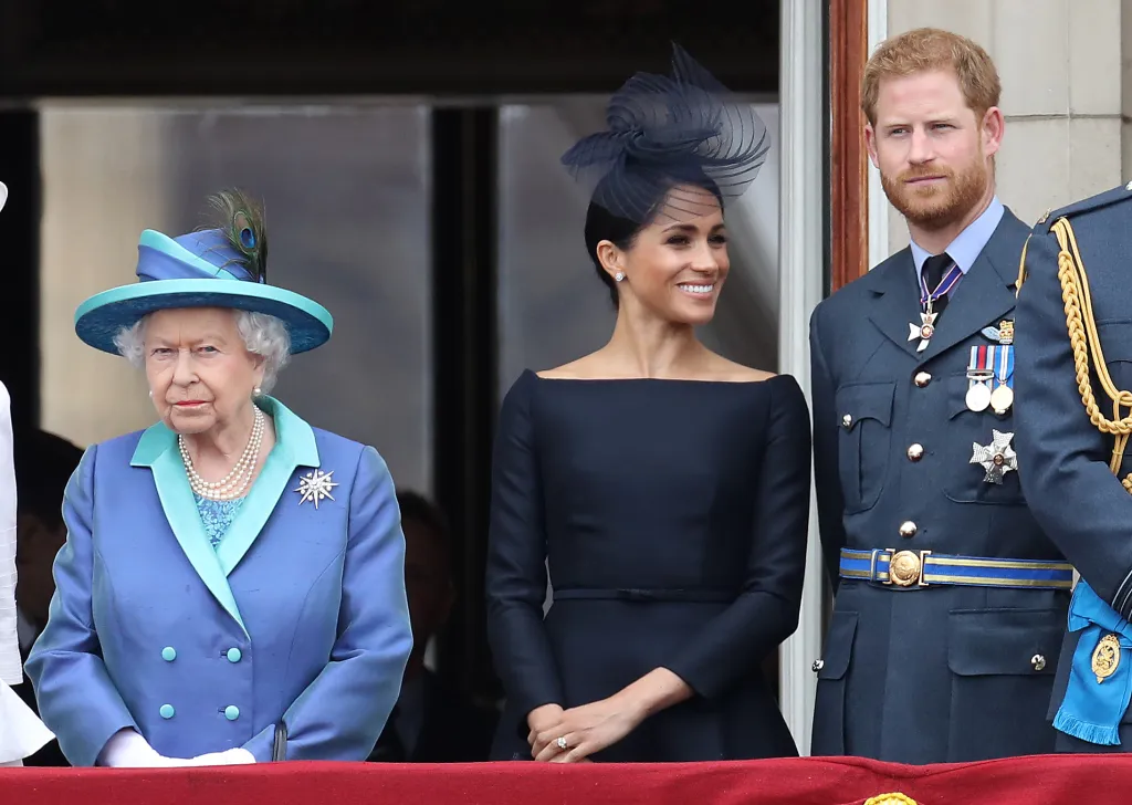 Queen Elizabeth II, Meghan Markle, and Prince Harry standing on a balcony at Buckingham Palace.