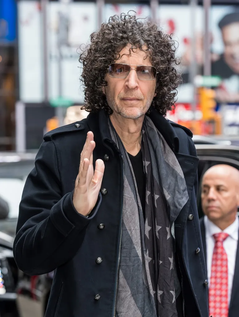 Radio and television personality Howard Stern walking with a man in a red tie behind him.