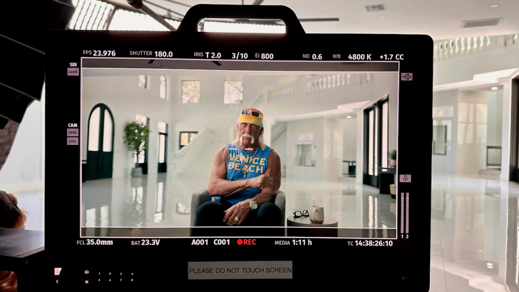 Hulk Hogan in a "Venice Beach" tank top, seated for an interview, as seen on a film production monitor.