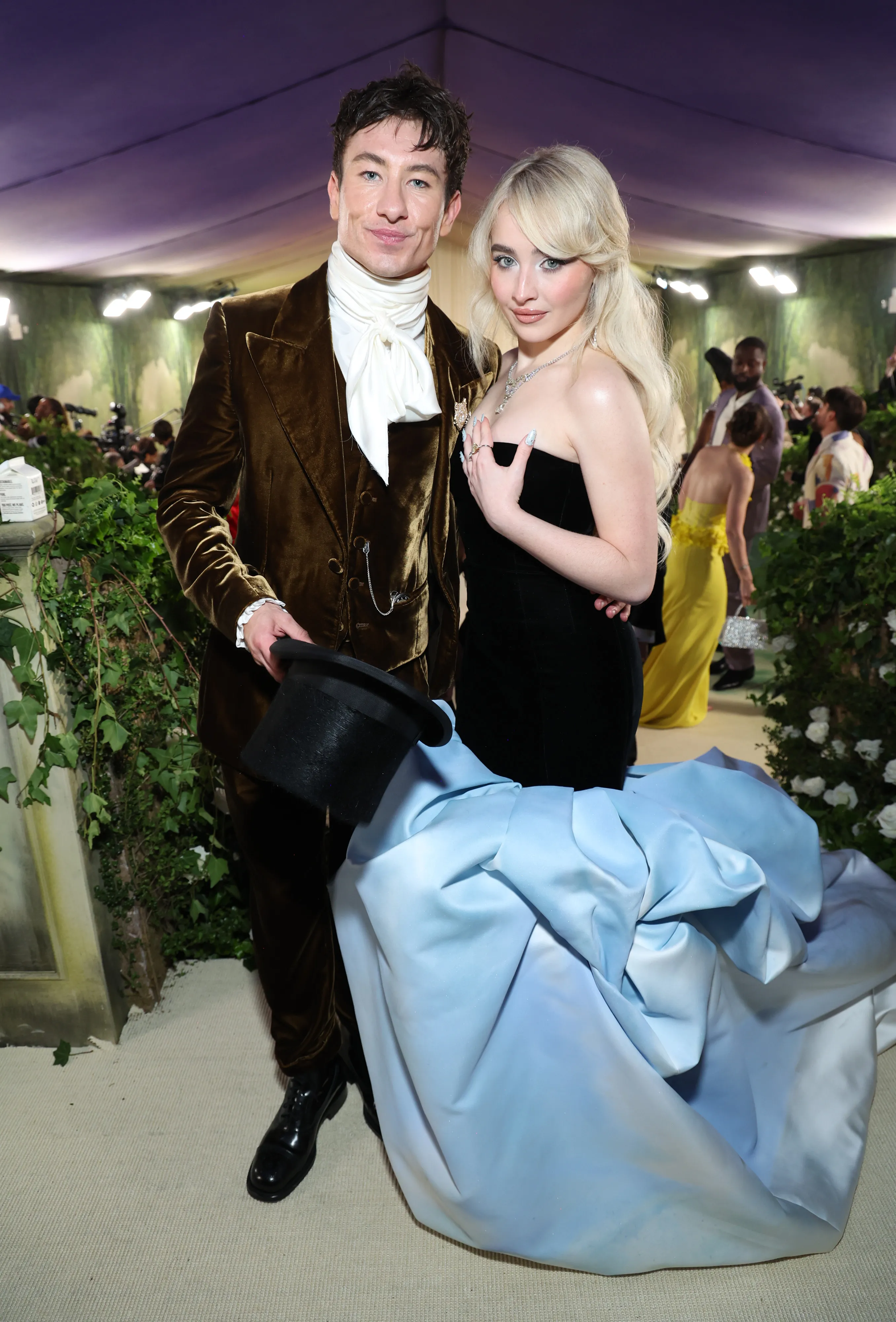 Barry Keoghan in a brown velvet suit with a white cravat and Sabrina Carpenter in a black strapless gown with a light blue and white ombré train.