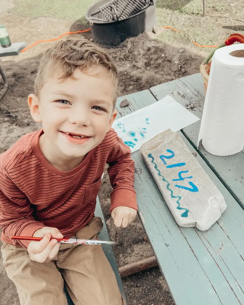 Reis Beck, a young boy, smiles while holding a paintbrush.