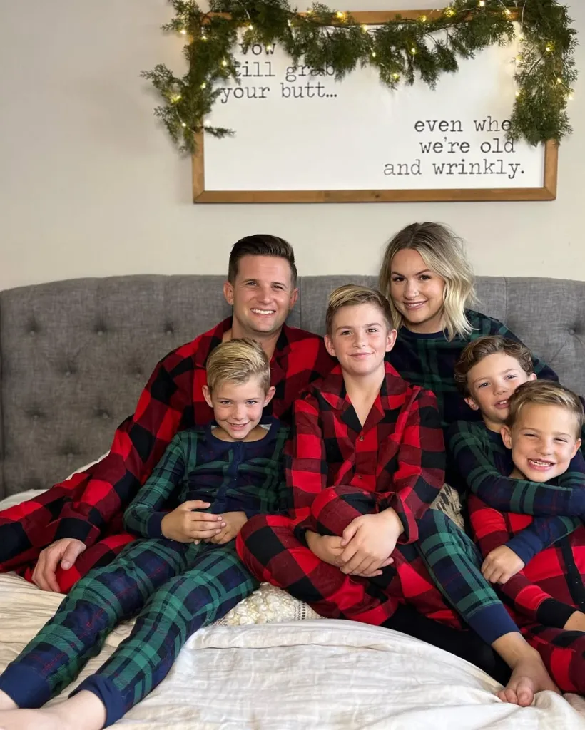 A family of five, including father Landon, mother Isabella, and their three sons, sits on a bed wearing plaid pajamas.
