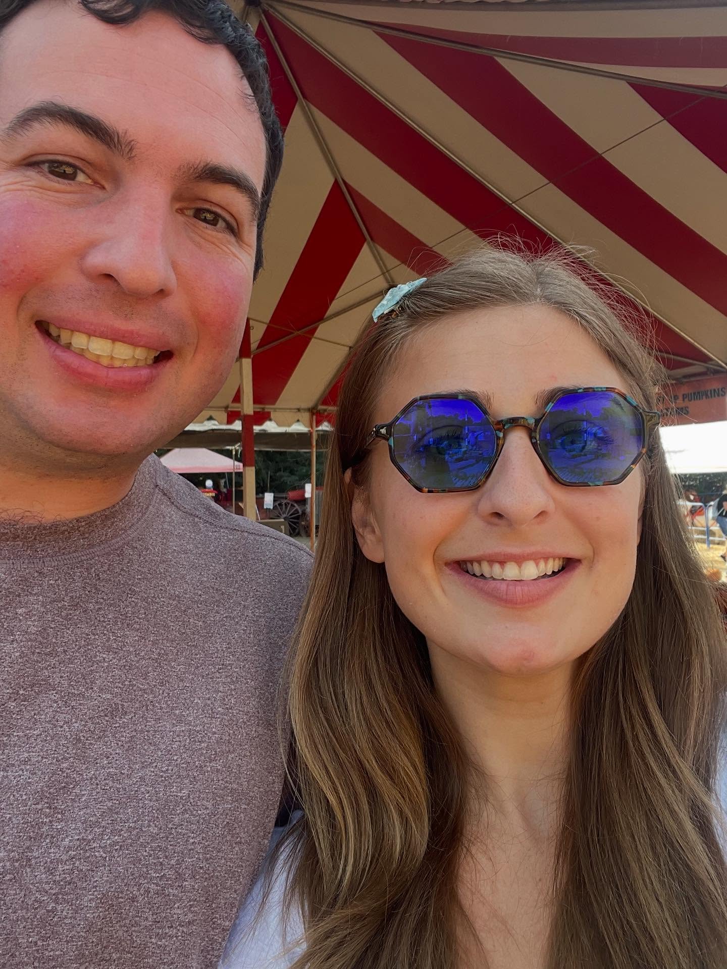 Abbey Romeo and David Isaacman smile at the camera, with a red and white striped tent behind them.