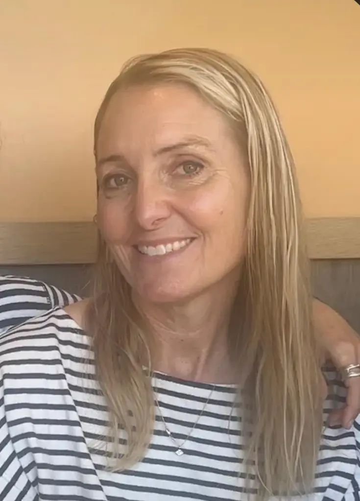 A 52-year-old white female, Amy Hillyard, with blonde hair and hazel eyes, wearing a black and white striped shirt.