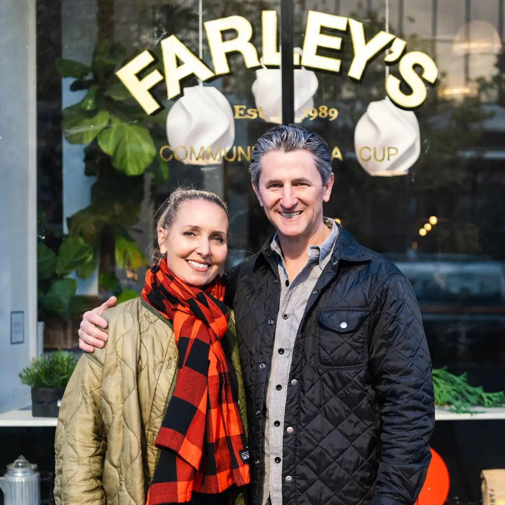 Amy Hillyard, a white woman with blonde hair and a red and black scarf, stands next to a man in front of a store.