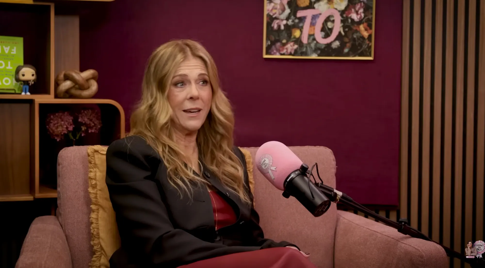 Rita Wilson seated in a chair on a TV set with a microphone.