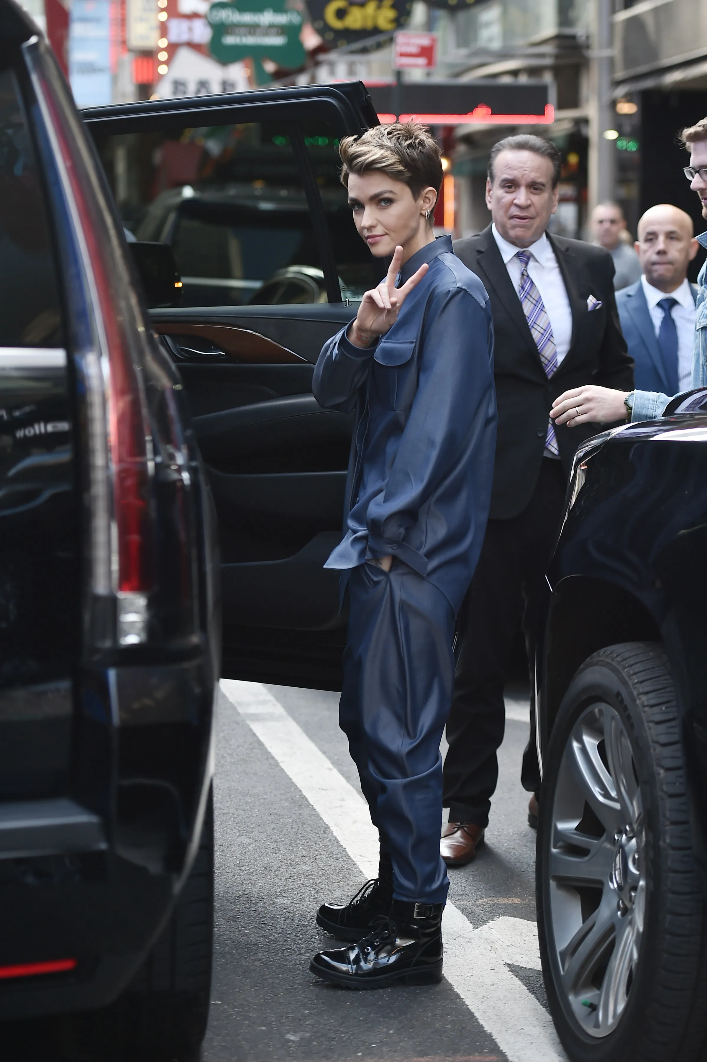 Ruby Rose in a blue outfit giving a peace sign while getting out of a car.