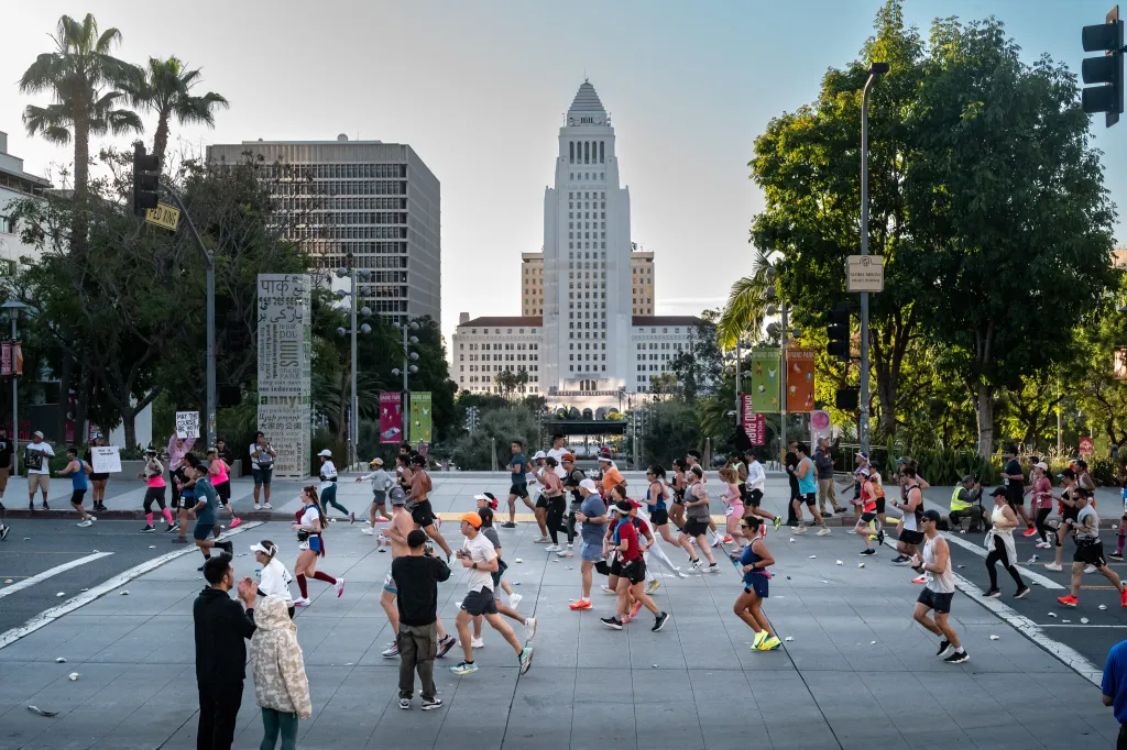 Runners participating in the Los Angeles Marathon on Grand Avenue, with City Hall visible in the background.