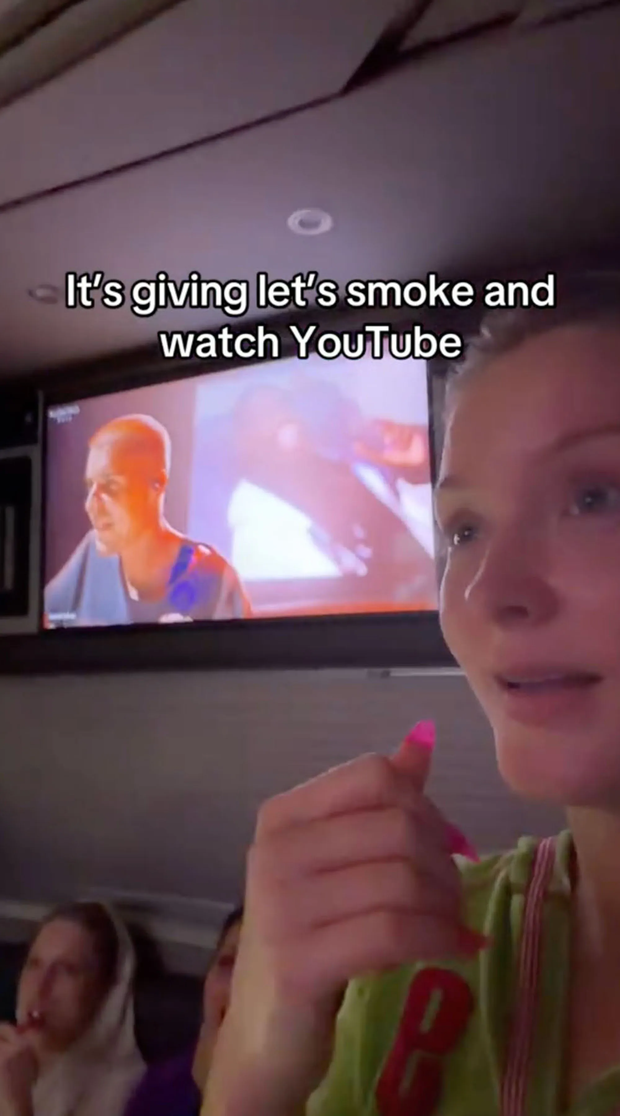 A young woman with bright pink nails points to a television screen playing YouTube, with text overlay 
