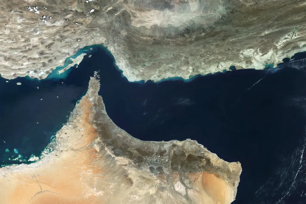 Satellite view of the Strait of Hormuz, connecting the Persian Gulf to the Gulf of Oman, with brown land on either side of the dark blue water.