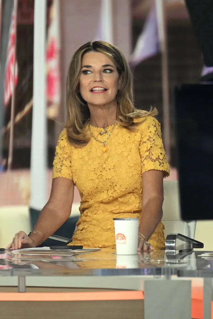 Savannah Guthrie in a yellow lace dress with a heart necklace, sitting at a desk with a "Today" show mug.