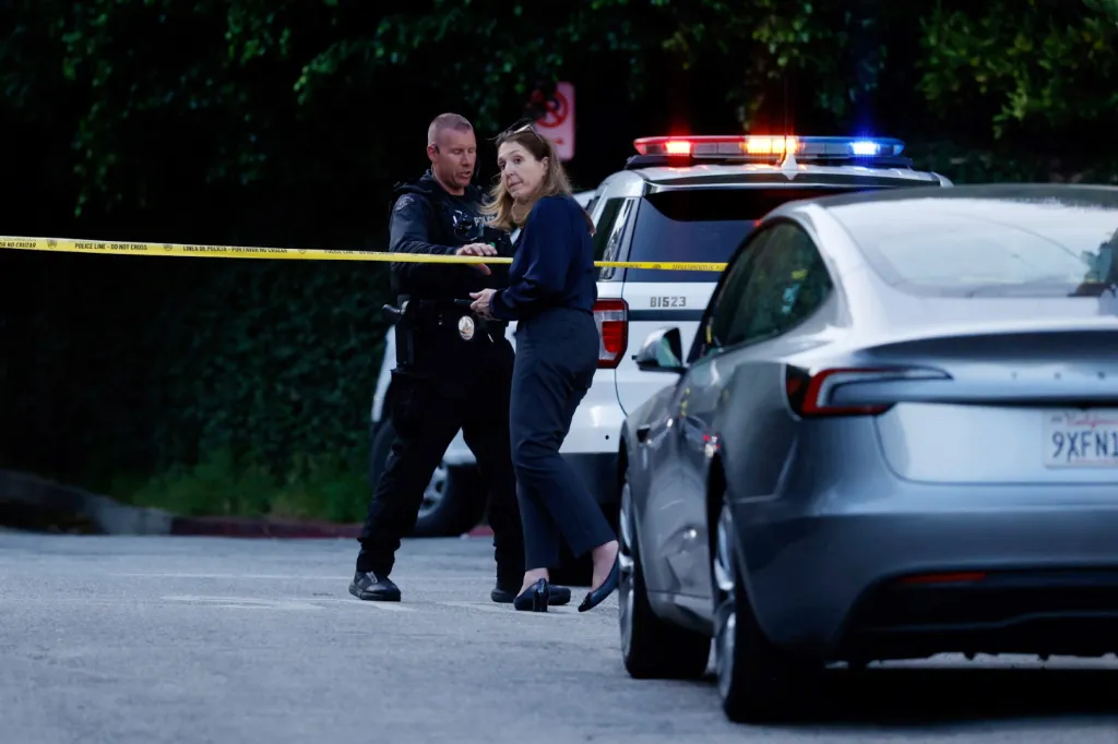 A police officer and a woman standing behind "Police Line - Do Not Cross" tape, with police vehicle lights flashing in the background.