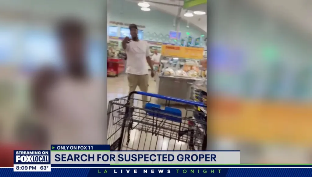 A man in a white t-shirt and baseball cap, suspected of groping a woman, is shown walking away in a grocery store as an empty shopping cart is visible in the foreground.