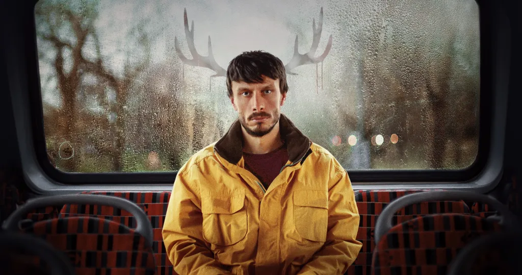 Richard Gadd as Donny Dunn, wearing a yellow jacket and sitting on a bus, with antlers superimposed above his head.