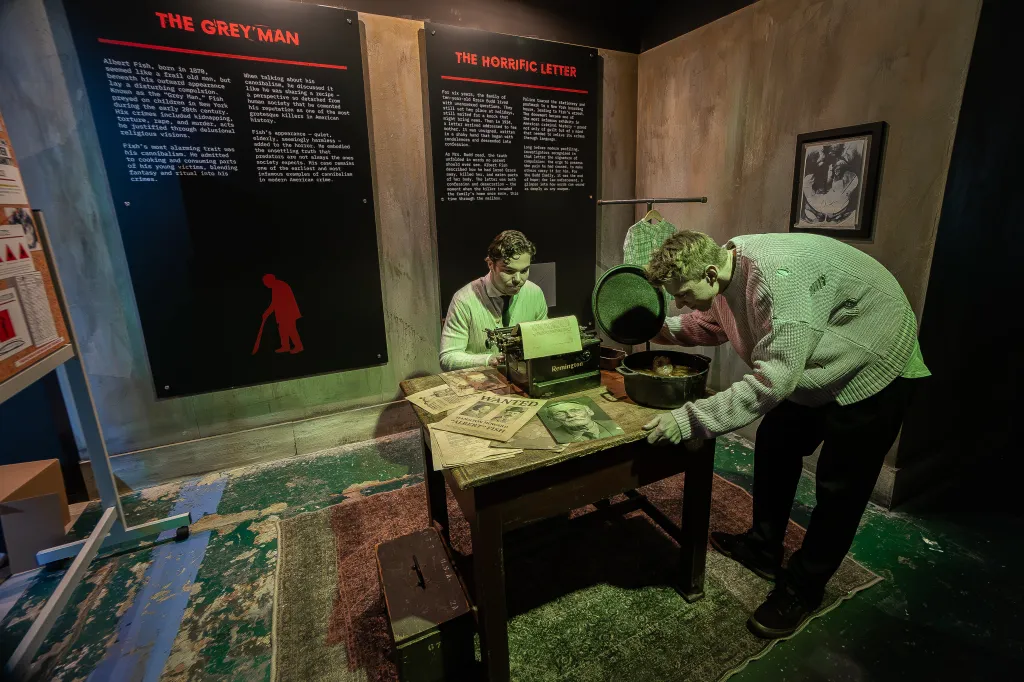 Exhibition with two mannequins, one typing and the other looking into a pot, with informational displays about "The Grey Man" and "The Horrific Letter" serial killer cases.