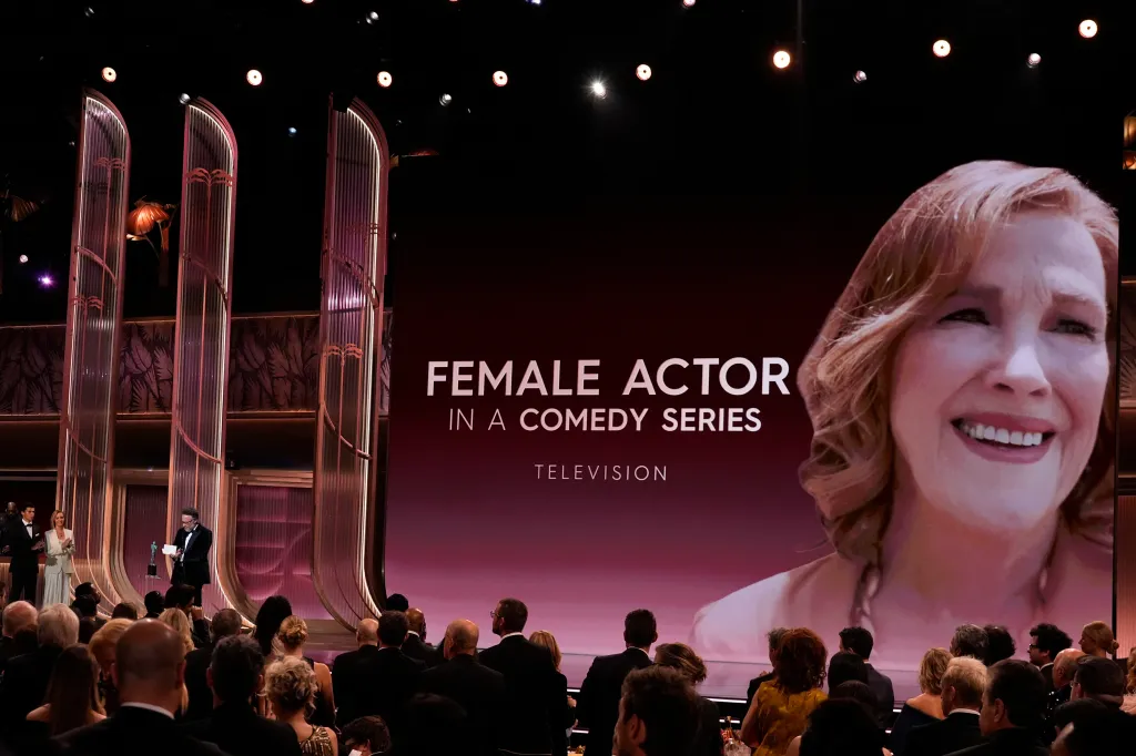 Seth Rogen accepts the award for outstanding performance by a female actor in a comedy series on behalf of Catherine O'Hara, while Lisa Kudrow watches from the left.