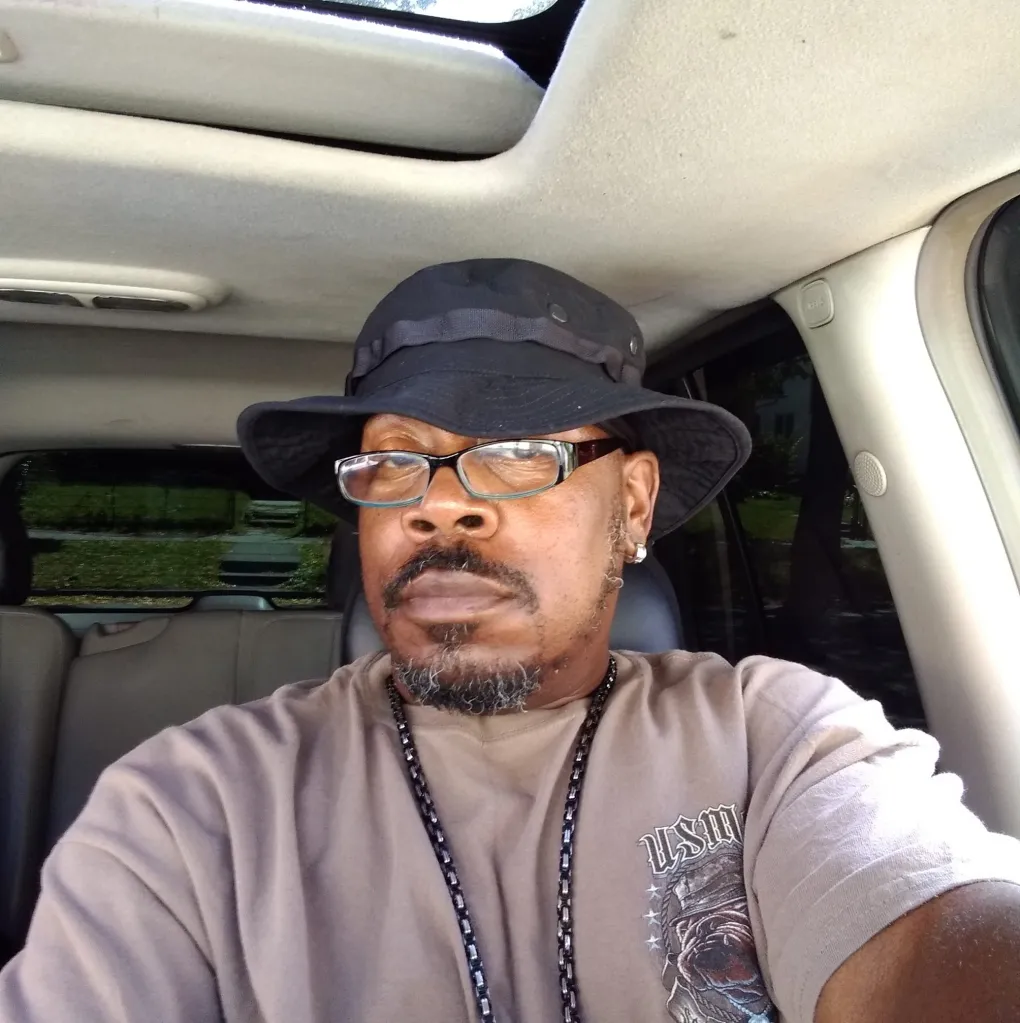 Horace Oates Jr. in a black hat and glasses, sitting in a car.