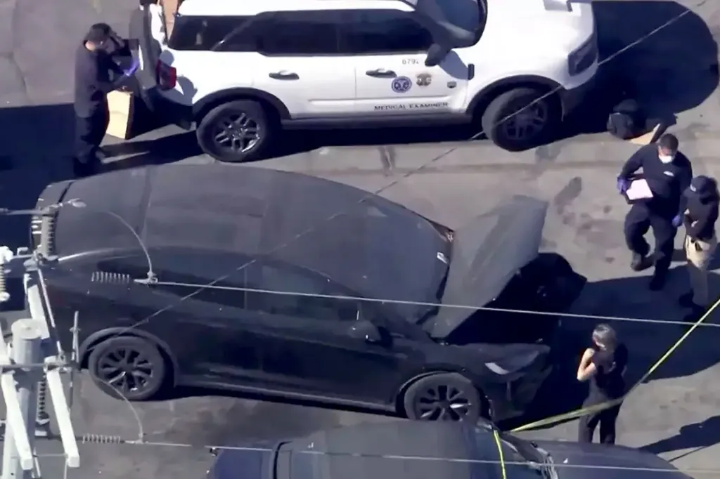 An aerial view of a black Tesla with its hood open and a white Medical Examiner vehicle parked behind it, with several people in work uniforms standing around the cars.