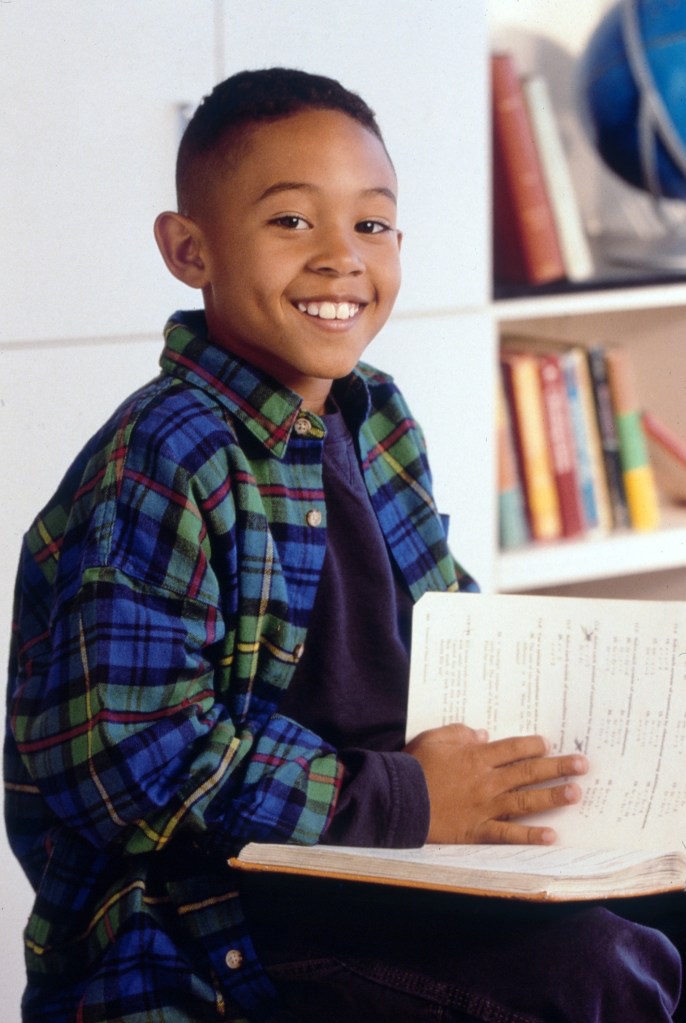 Portrait of Tahj Mowry from the TV series "Smart Guy", sitting in a classroom and holding a textbook.