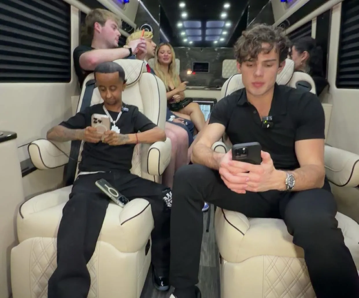 People sitting in a vehicle, with two men in the foreground looking at their phones.
