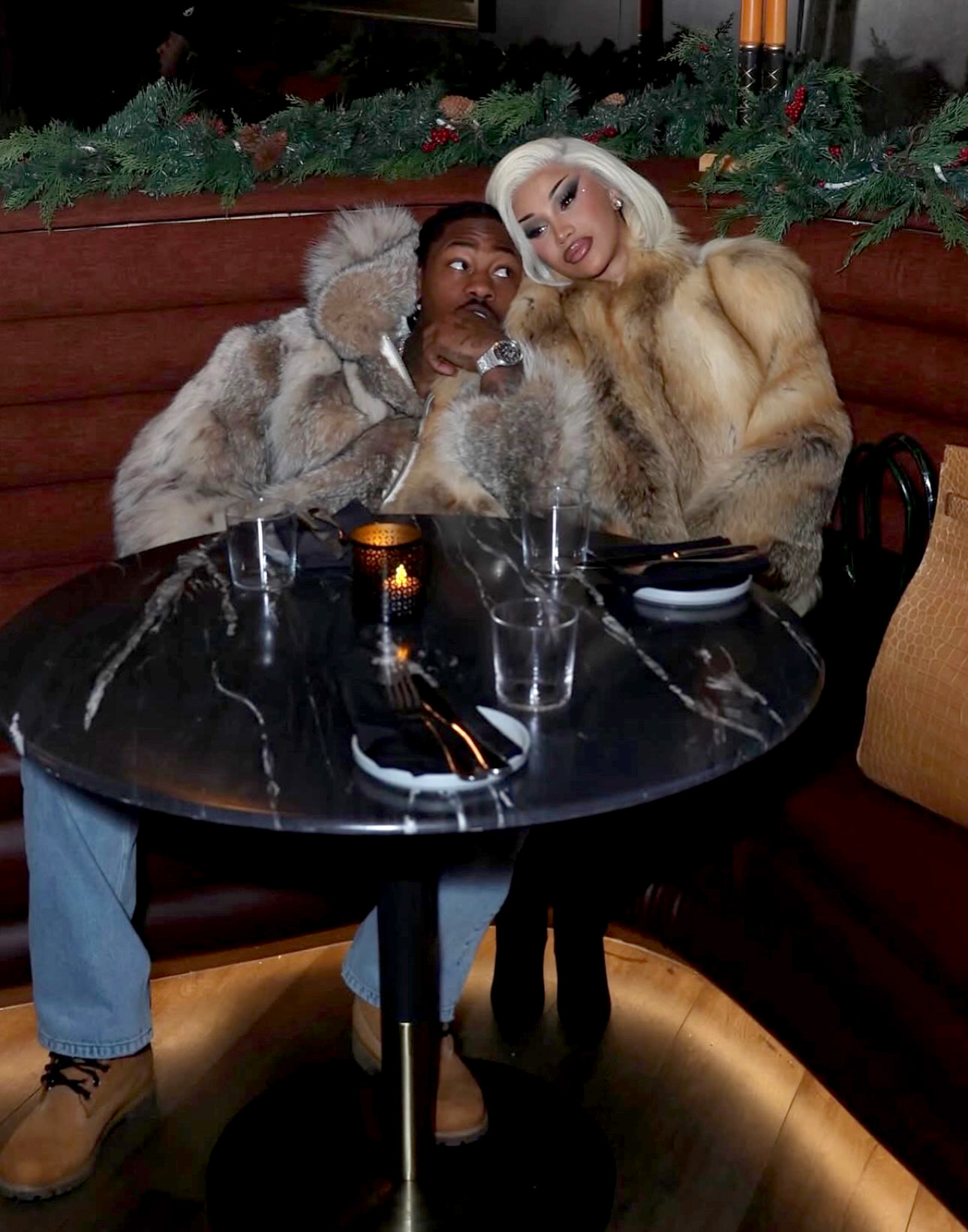 Stefon Diggs and Cardi B seated at a table, both wearing fur coats.
