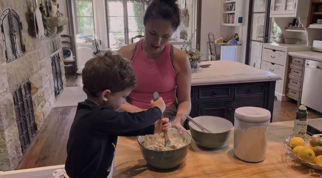 Mehgan Markle, in a pink top, cooks with Prince Archie, in a black top and a white apron.