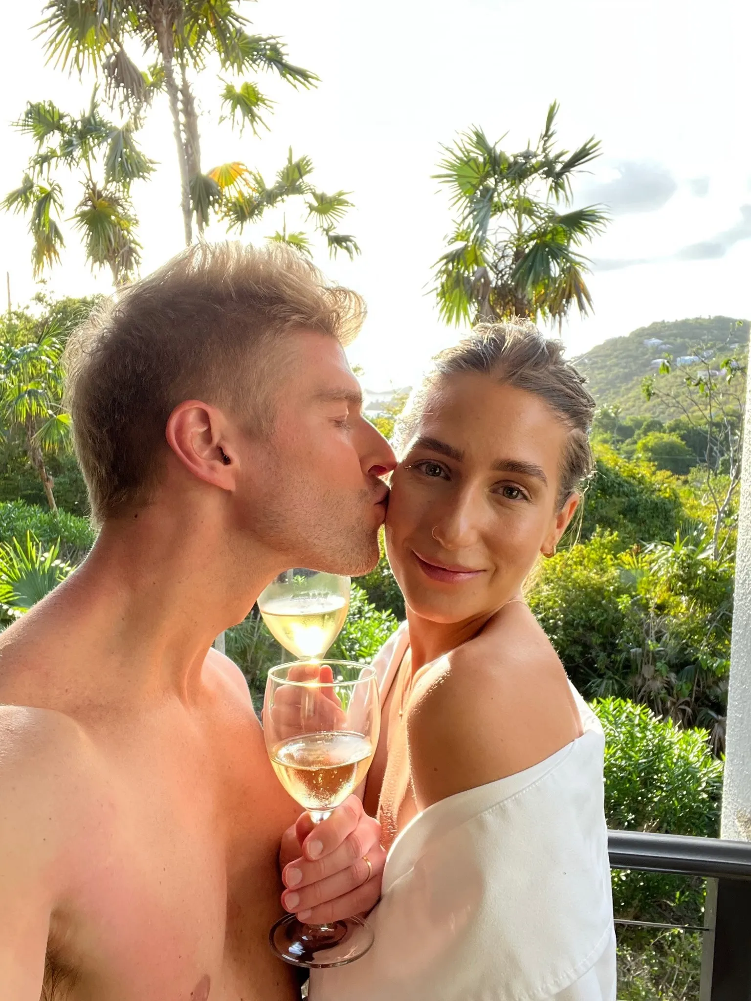 Kyle Cooke kissing Amanda Batula on the cheek as they hold glasses of white wine.