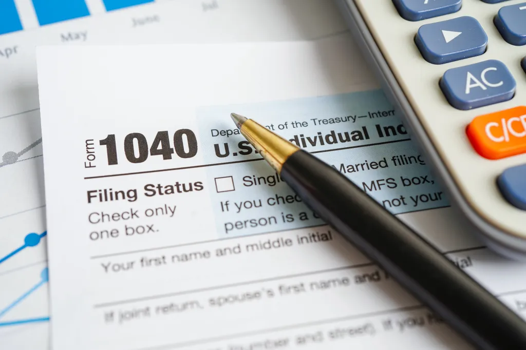 Tax Form 1040, a pen, and a calculator on a financial graph.