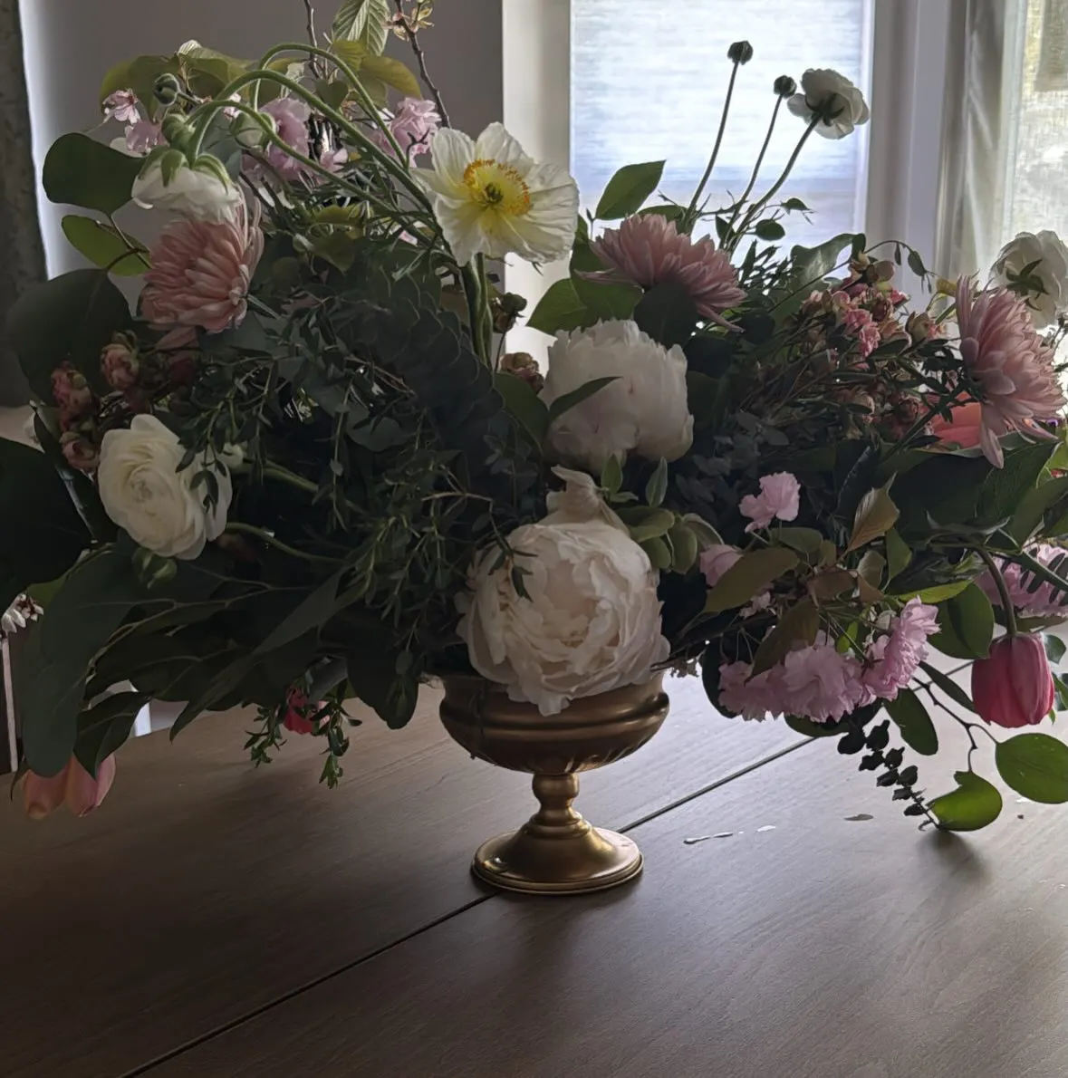 A large floral arrangement in a gold vase on a wooden table.