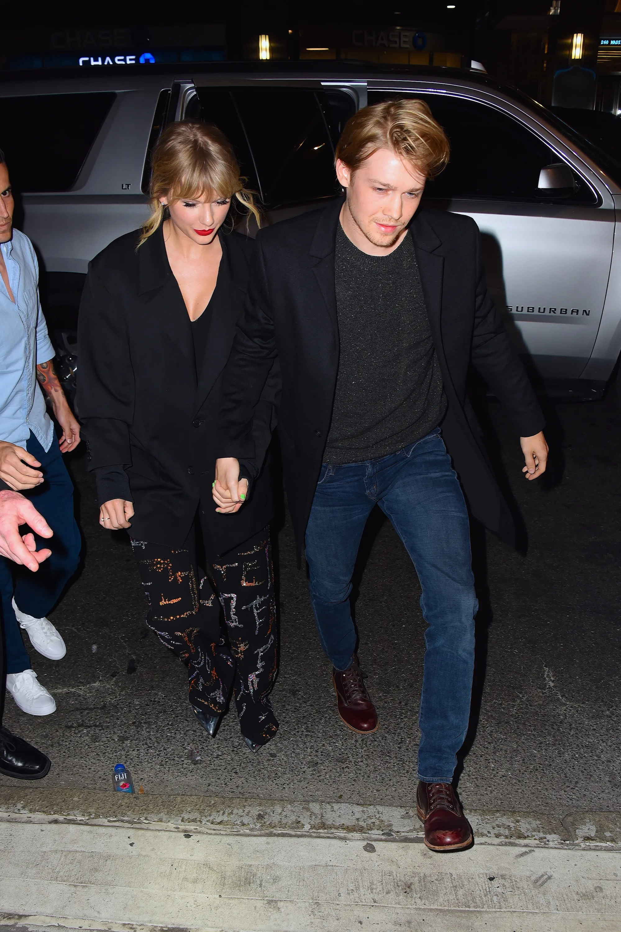 Taylor Swift and Joe Alwyn hold hands while walking together at night.