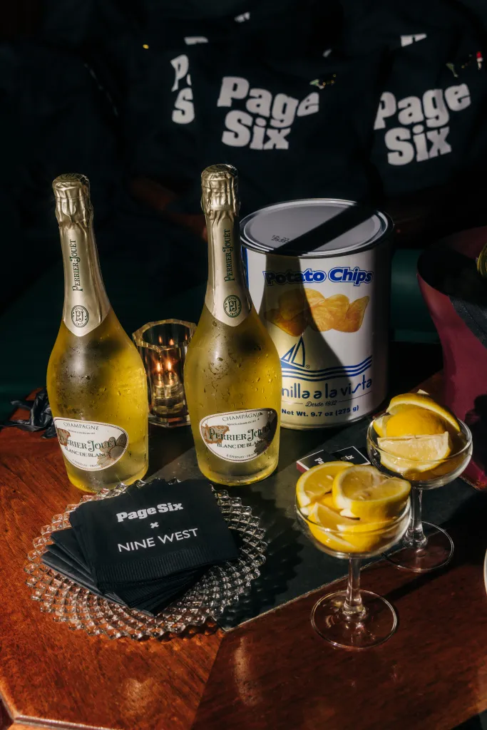 Table setup with champagne, potato chips, and Page Six x Nine West napkins for an event.