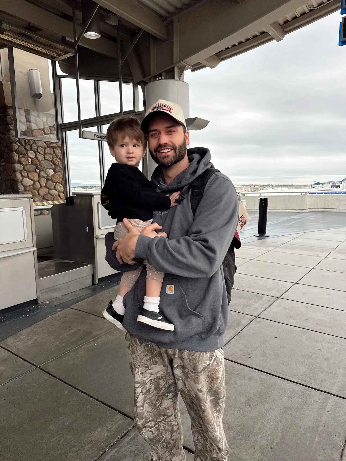 Dakota Mortensen holding his son Ever at an airport.