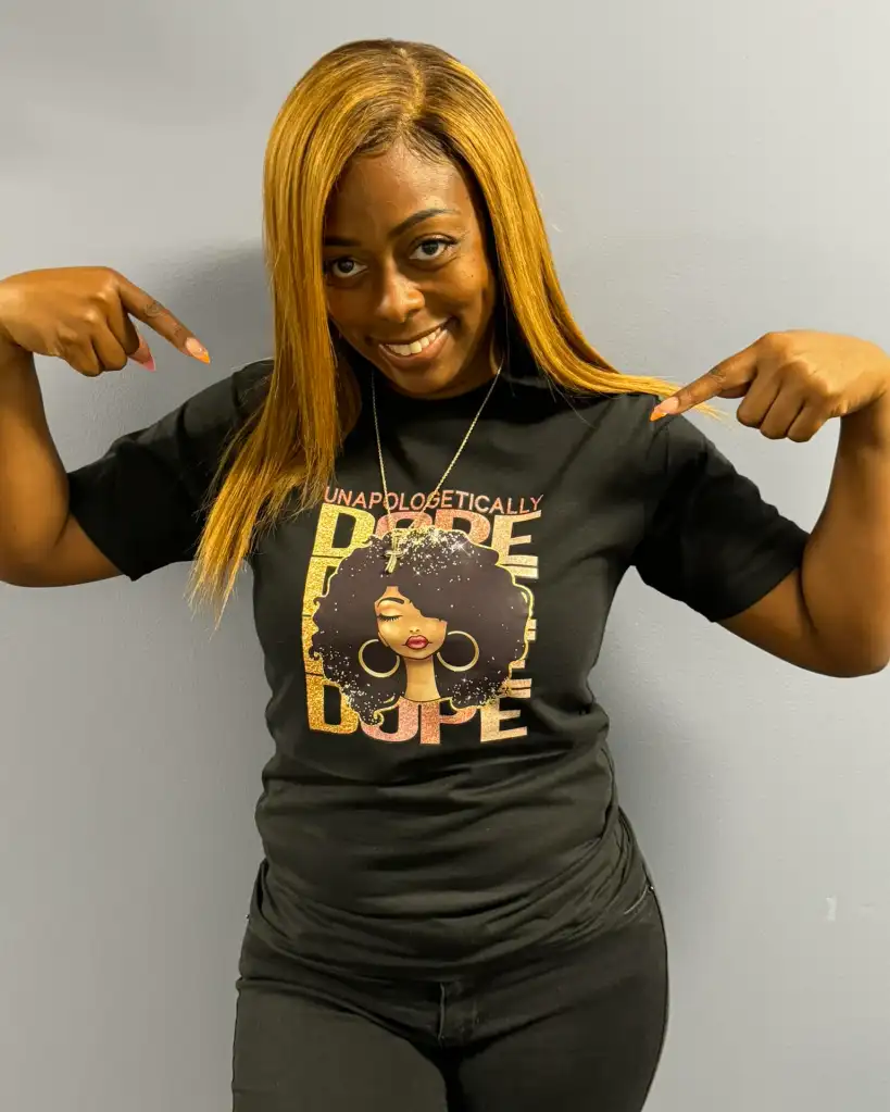 Dolton, Illinois Mayor Tiffany Henyard pointing to her black t-shirt that says "UNAPOLOGETICALLY DOPE" with an illustration of a woman.