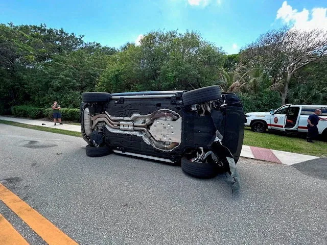 A Land Rover SUV overturned on a road, with emergency personnel nearby.