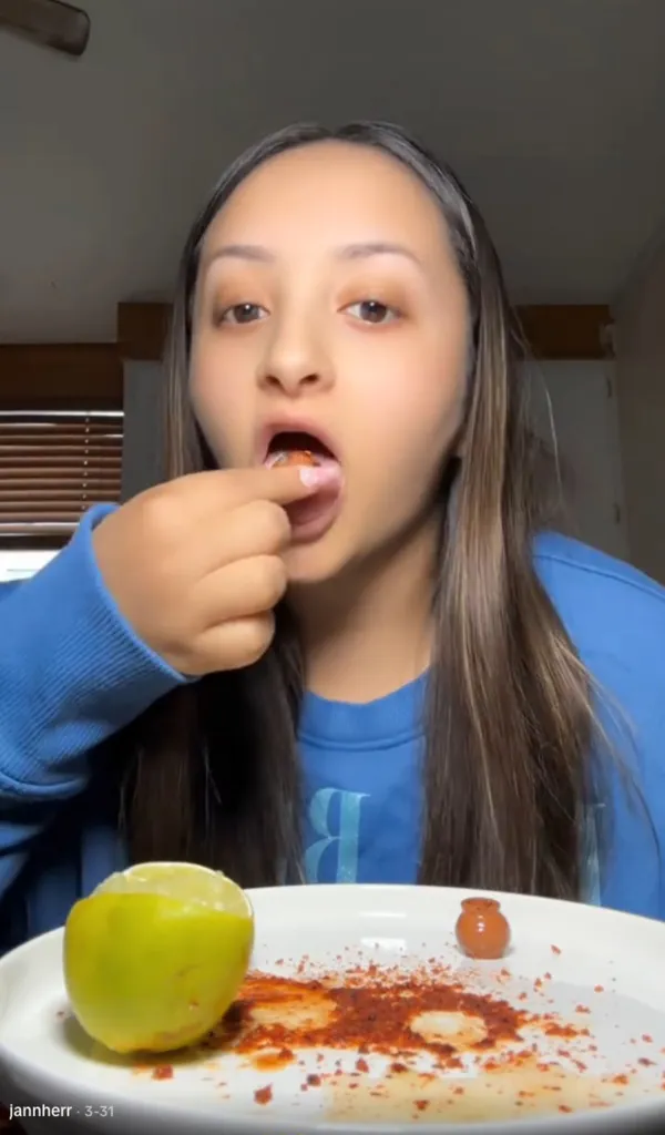 A woman eats a small clay pot after dousing it in lime and Tajin.