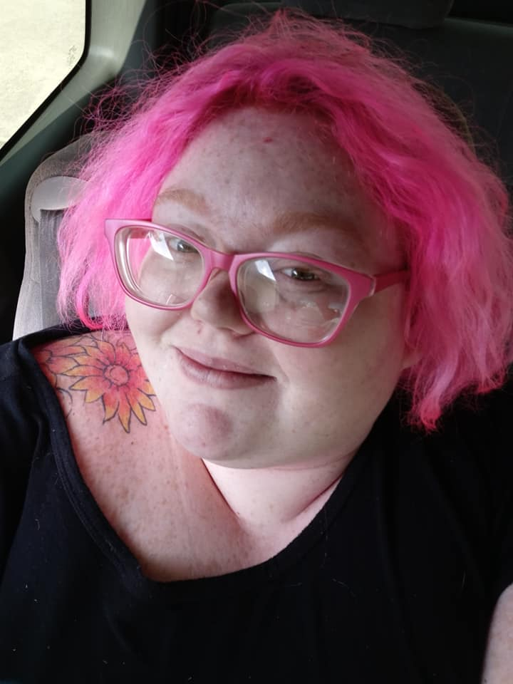 Dolly Martinez, a woman with bright pink hair, glasses, and a sunflower tattoo on her shoulder.