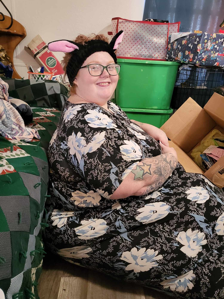 Dolly Martinez sits smiling, wearing a black floral dress and bunny ears, with a Christmas quilt next to her.