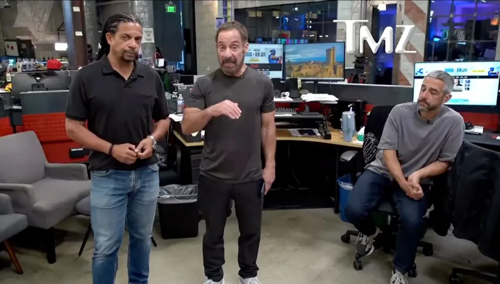 Three men, two standing and one seated, in an office environment with the TMZ logo visible.