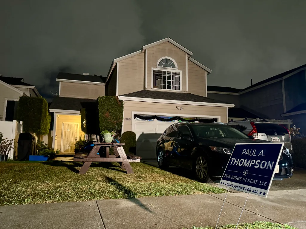 Nighttime view of a two-story house with a "Paul A. Thompson for Judge" campaign sign in the foreground.