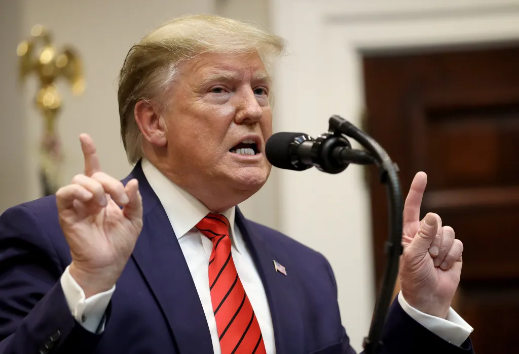 U.S. President Donald Trump speaking at a podium with two fingers raised.