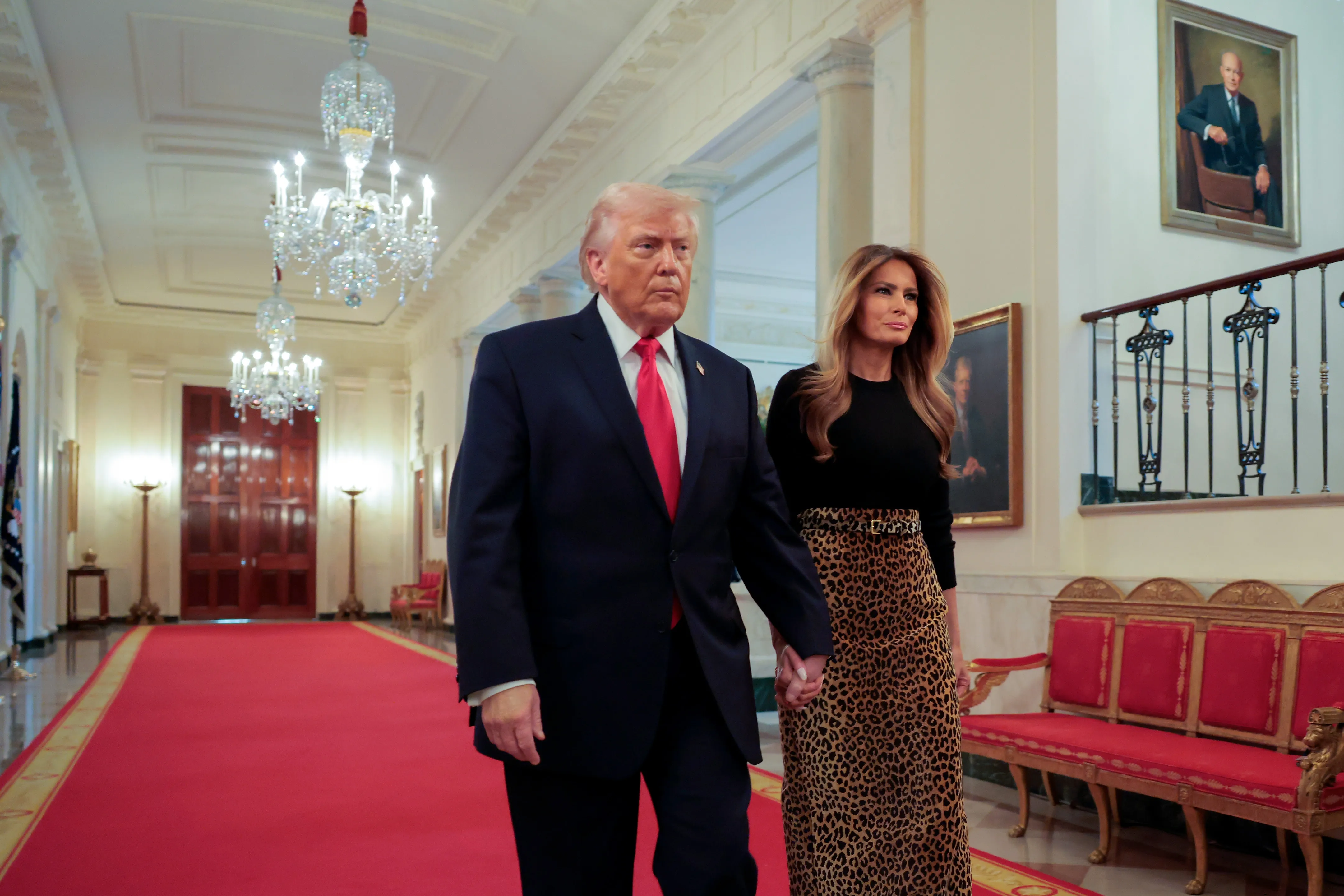 Donald and Melania Trump walk hand-in-hand down a red carpet hallway at the White House.
