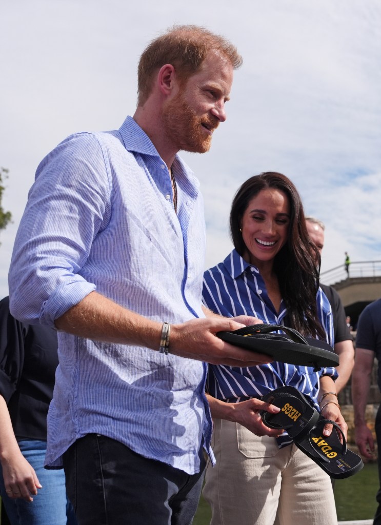 Prince Harry and Meghan Markle holding flip-flops presented to them, one with 