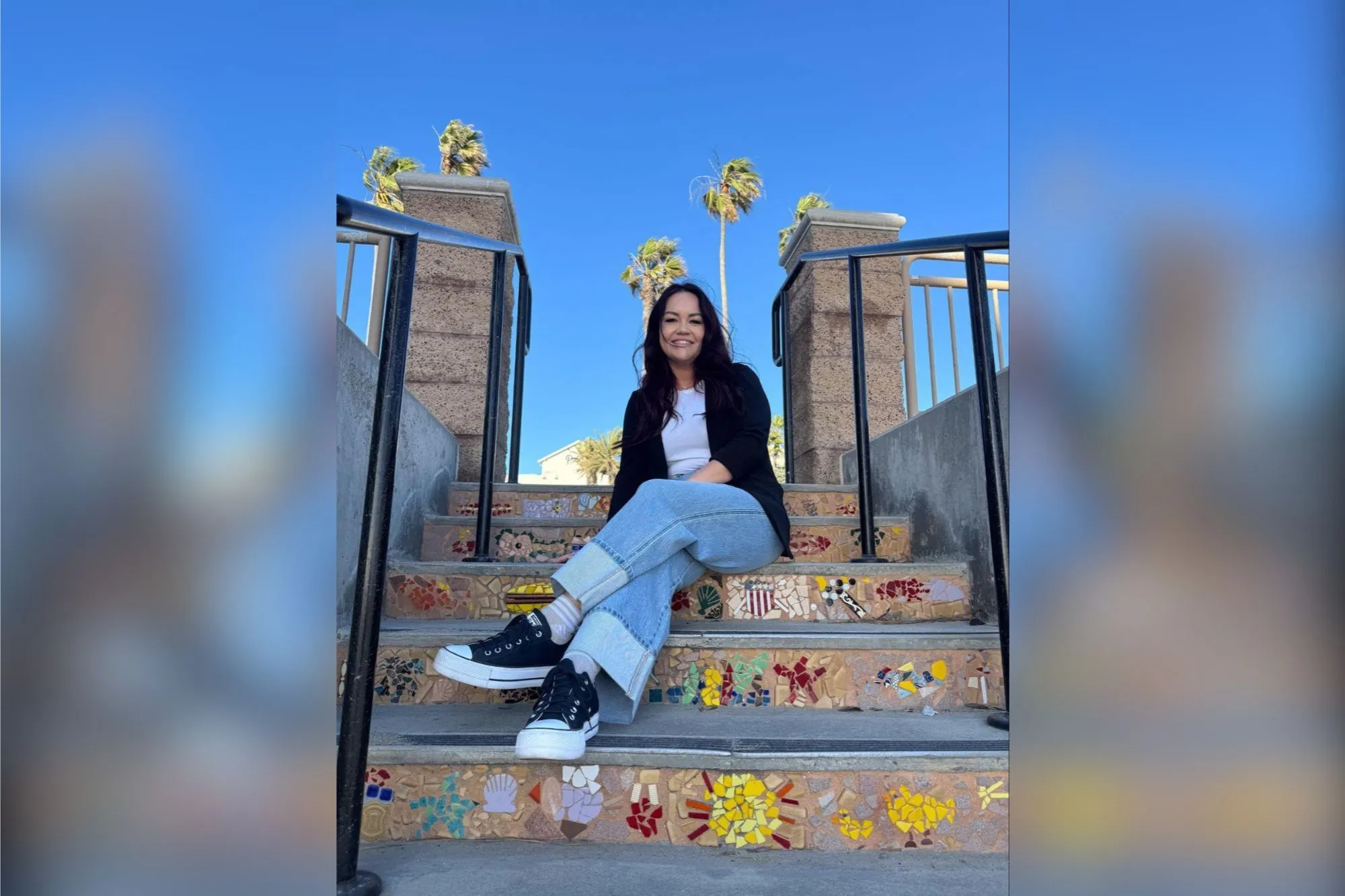 Bree Mesquit, owner of Rebel Wax, smiles while sitting on mosaic steps under a clear blue sky.