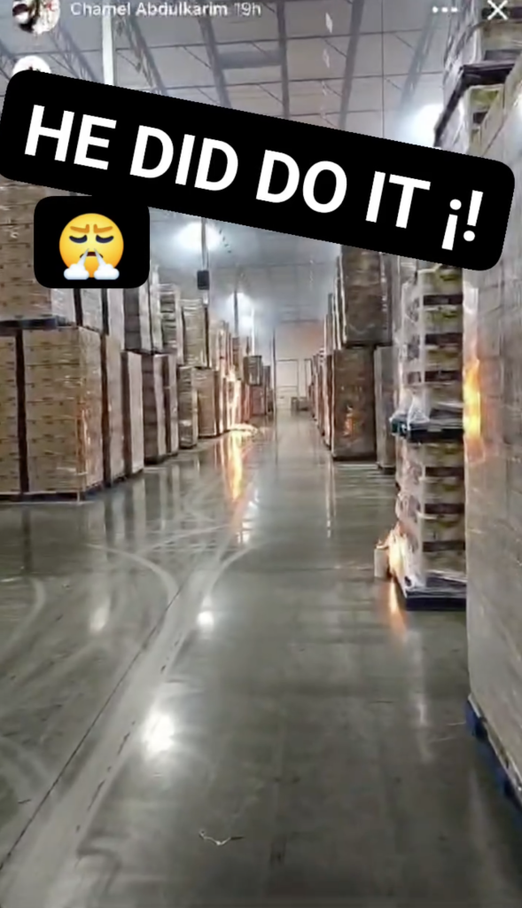 Video frame showing an aisle in a warehouse with stacked pallets and flames visible on the right.