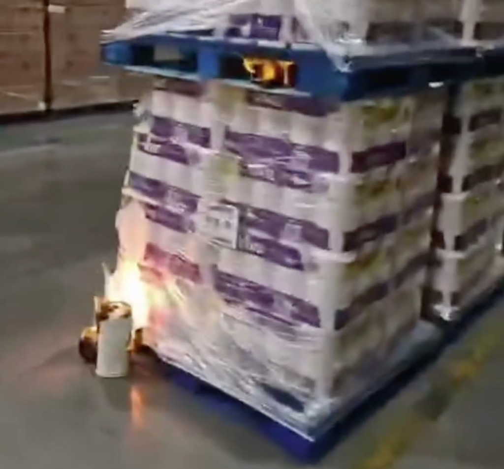 A fire burning next to a pallet of toilet paper rolls wrapped in plastic.
