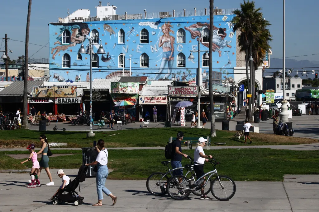 A light-blue building with a large mural and arc-shaped windows, and a street scene with people walking and riding bikes at Venice Beach, Los Angeles.
