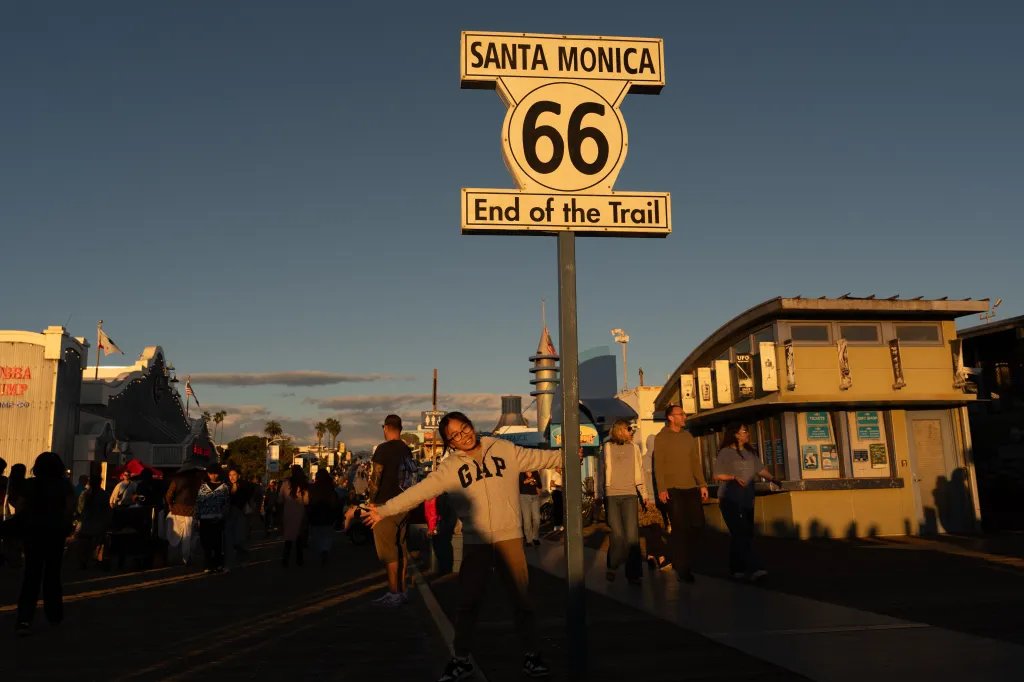 A visitor poses for photos with the "End of the Trail" Route 66 sign on the Santa Monica Pier.