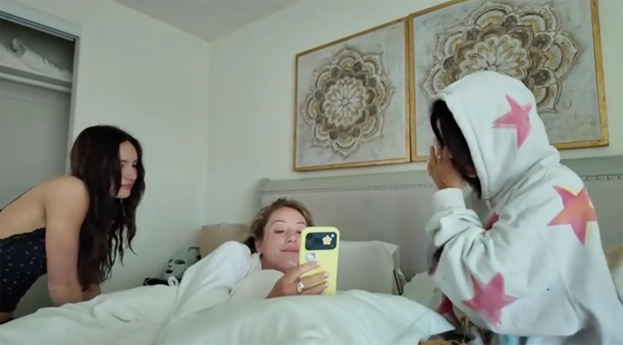 Alix Earle watching a video on a phone while laying in bed, with two other people.