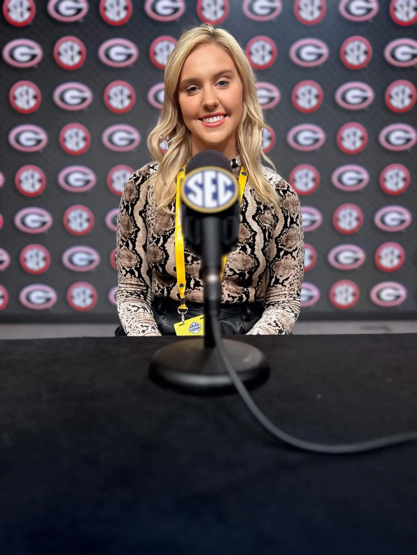 NFL reporter Crissy Froyd smiling in front of a microphone with a backdrop of Georgia Bulldog and SEC logos.